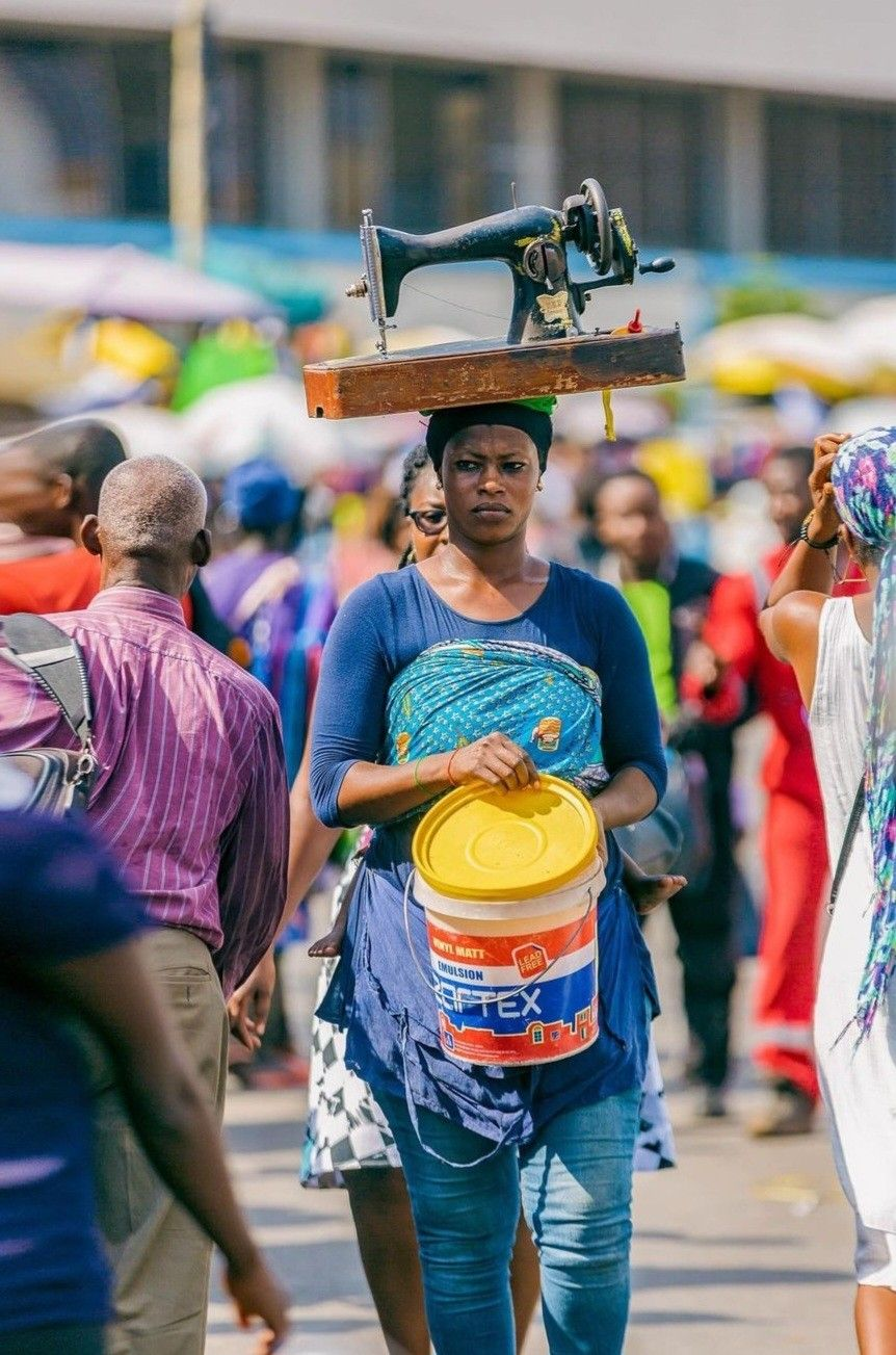 A woman carrying a sewing machine on her head through a crowded market